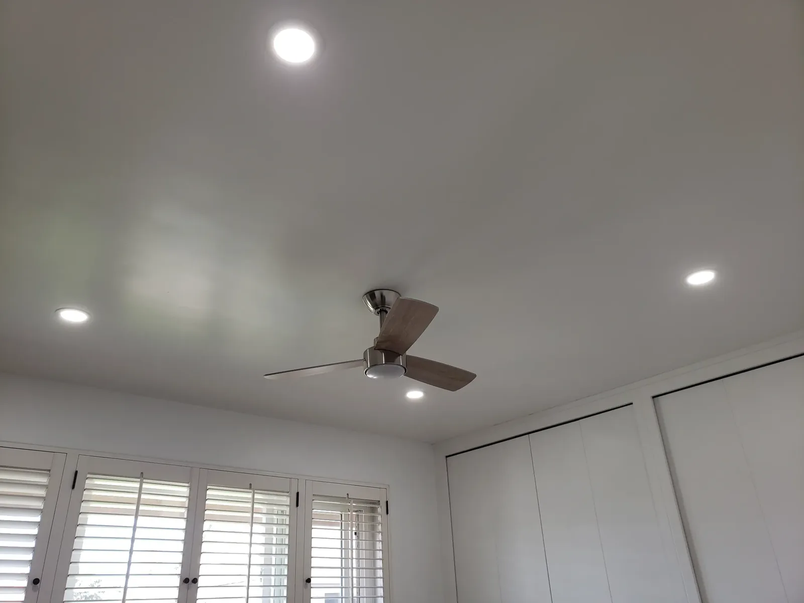 Recessed ceiling lights and modern ceiling fan installed in a bright room